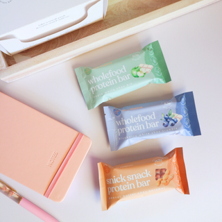 A selection of The Wholefoods Protein Bars artfully arranged with books on a desk, emphasizing their role as a delicious and nutritious snack option for busy individuals seeking a healthy boost during study or work sessions