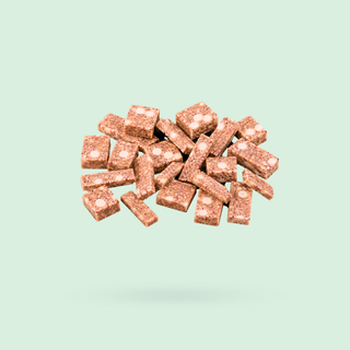 A pile of small rectangular apple white choc pie protein bar pieces floating against a solid pale green background.