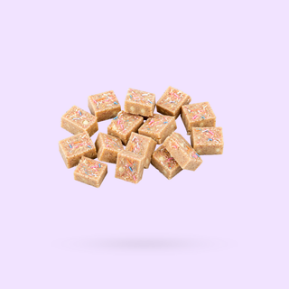 A pile of small square birthday cake protein bars pieces with colorful sprinkles, floating against a light lavender background.