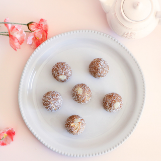 Five Carrot Cake Protein Balls on a white plate with pink flowers and a teapot in the background.