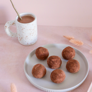 Chocolate Malt Protein Balls on a plate with a mug of hot chocolate