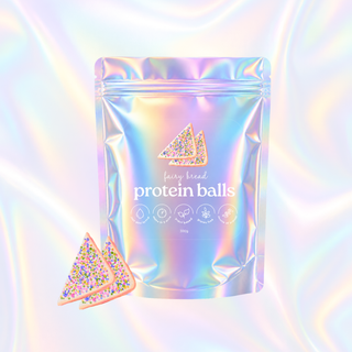 A stand-up pouch of fairy bread protein balls with a holographic iridescent finish, shown on a matching wavy pastel background with two triangular protein ball pieces displayed in front.