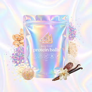 An iridescent holographic stand-up pouch labeled 'fairy bread protein balls' centered on a pastel rainbow background, surrounded by loose ingredients including nuts, sprinkles, oats, vanilla bean, and a protein ball.