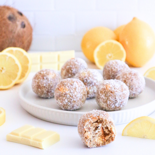 Lemon Protein Balls on a plate with lemons and white chocolate bars in the background