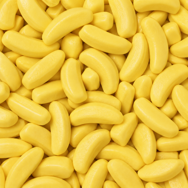 A close-up, top-down view of many small, glossy yellow banana-shaped candies or gummy candies filling the entire frame.