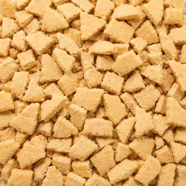 A close-up, top-down view of numerous small, irregularly shaped golden-brown snack cookie crumbs filling the frame.