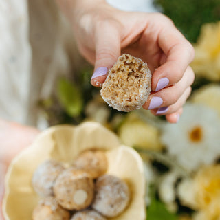 Hand holding a lemon cheesecake protein ball with a blurred floral background
