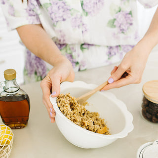 Person in a floral outfit mixing protein ball mix in a bowl on a light surface.