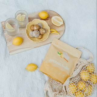 Picnic setup with lemons, a basket of flowers, and a book on a light blue blanket.
