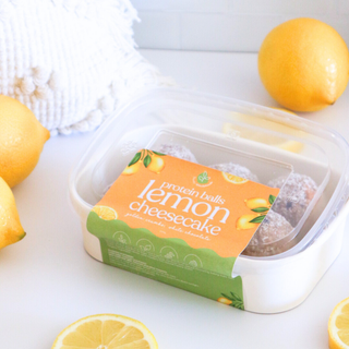 Container of lemon cheesecake protein balls with lemons on a white surface