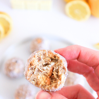 Hand holding a lemon cheesecake protein balls with lemons in the background