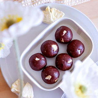 White dish with pineapple chocolate protein balls on a light wooden surface with flowers.