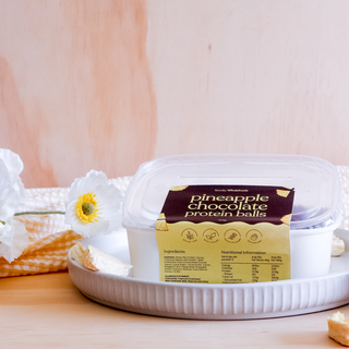 Container of pineapple chocolate protein balls on a white plate with flowers in the background