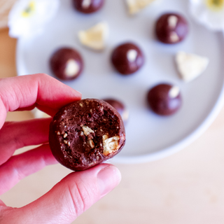 Hand holding a pineapple chocolate protein ball with a plate of more in the background.
