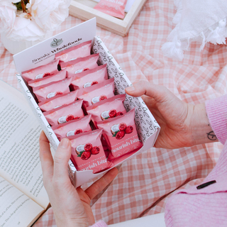 Box of raspberry lamington nourish bites held by a person on a pink checkered background