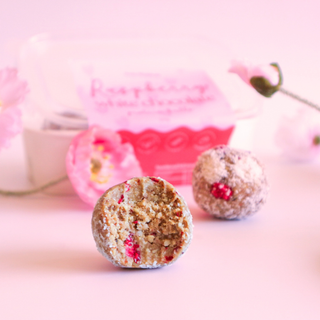 Two round, textured protein balls with raspberries on a pink background