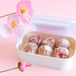 Container of Raspberry White Chocolate Protein Balls with pink flowers on a pink background
