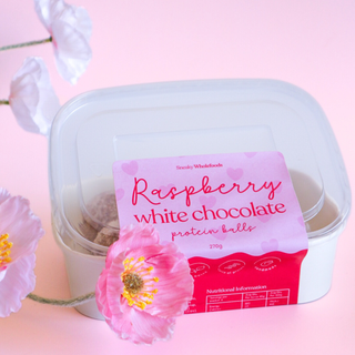 Container of raspberry white chocolate protein balls with pink flowers on a pink background