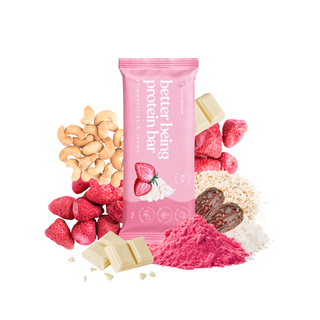 A pink package labeled 'better being protein bar' stands upright on a white background, surrounded by ingredients including cashews, strawberries, white chocolate pieces, pea protein dates, and beetroot powder.