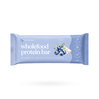 A single wrapped protein bar package on a clean white background. The wrapper is light blue with white text reading 'wholefood protein bar' and 'blueberry white choc crumble,' plus a blueberry illustration and small icons on the right.