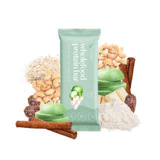 A green Apple White Choc Pie Wholefood Protein Bar package centered on a white background, surrounded by ingredient illustrations including cashews,  green apples, cinnamon sticks, dates, and pea protein