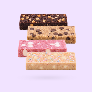 Four protein bars in different flavours arranged in a row on a white background: Hazelnut choc fudge , vanilla cookie dough, strawberry cream, and birthday cake flavours. 