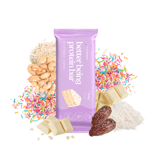 A purple wrapper package labeled birthday cake better being protein bar stands upright on a white background, surrounded by chocolate pieces, cashews, dates, sprinkles, and pea protein