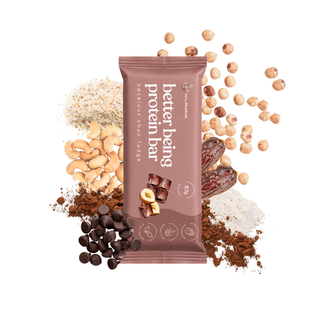 A single protein bar package stands upright on a white background, surrounded by scattered nuts, chocolate pieces, and powder. The package is mauve-brown with white text reading 'Hazelnut Choc Fudge better being protein bar"