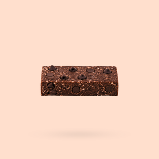 A single jaffa choc chip nourish bite with embedded chocolate chips, centered against a solid pale peach background.