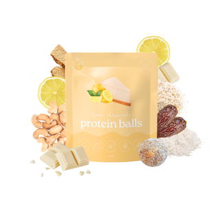 A stand-up pouch of lemon cheesecake protein balls centered on a white background, surrounded by ingredient props including lemon slices, chocolate pieces, dates, nuts, and a coated protein ball.