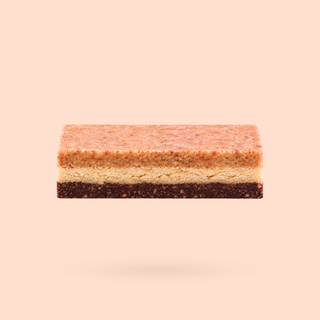 A rectangular layered peanut butter caramel snack bar with three horizontal layers, shown floating against a solid pale peach background.