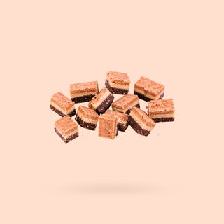A cluster of small rectangular layered snacks or cookies with a golden-brown top and dark brown base, floating against a solid pale peach background.