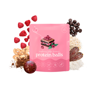A pink stand-up pouch labeled 'protein balls' with a raspberry cake illustration, surrounded by loose ingredients including raspberries, chocolate chips, cashews, cocoa powder, dates, and a protein ball on a white background.