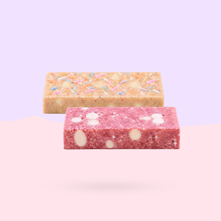 Two rectangular protein bars, one in light tan with pastel sprinkles and one in strawberry pink with white chunks, shown on a white background.