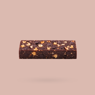 A single chocolate hazelnut protein bar with visible hazelnuts and chocolate chips, centered against a solid dusty pink background.