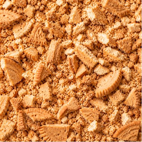 A close-up texture shot of crushed golden-brown biscuits or cookies, showing both fine crumbs and larger broken pieces with embossed patterns.