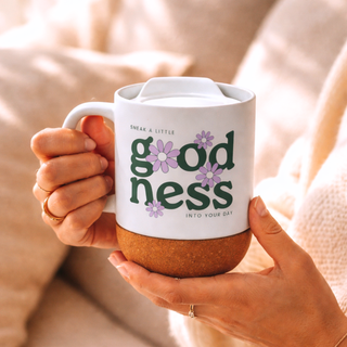 Person holding a mug with 'goodness' text and flowers design.