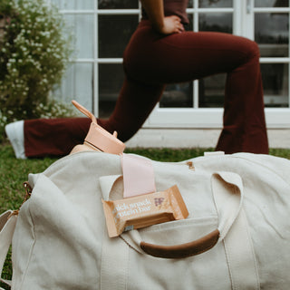 Close-up of Sneaky Wholefoods Peanut Butter Caramel Snick Snack Protein Bar in a gym bag, with a woman stretching in the background, ideal for a post-workout, high-protein boost.