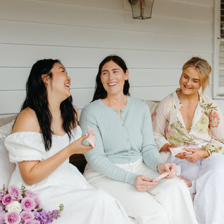 Work friends laughing and enjoying Sneaky Wholefoods Vanilla Cookie Dough Protein Bars during a snack break on a bench, celebrating tasty and nutritious snacking together.