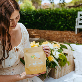 Sunny afternoon picnic with Lemon Cheesecake Protein Ball on a platter with glasses of water, lemons all placed on a white picnic rug